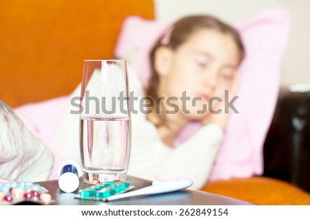 Medicines and glass of water for ill sleeping child lying on a sofa. Indoors.