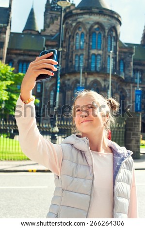 Cheerful young beautiful girl taking picture with smartphone in Glasgow historical place. Traveling. Summertime outdoors.