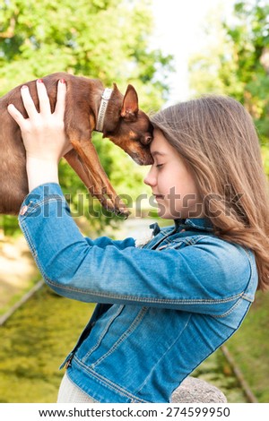 Unconditional love. Teenage girl with brown toy-terrier dog. Multicolored summertime outdoors image.