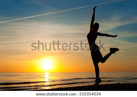 Enjoying the summer evening. Cheerful slender woman silhouette dancing on the sunset with raised up hands on blue sky background on the beach. Summertime multicolored outdoors horizontal image.
