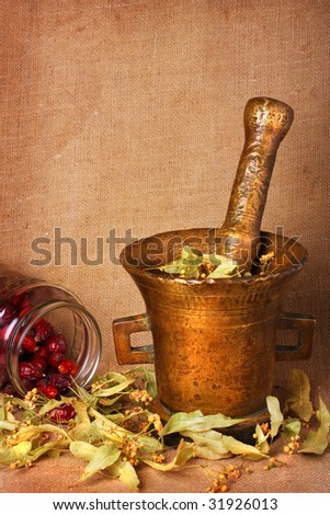 Old bronze mortar with dry herbs and rose hips on sacking background
