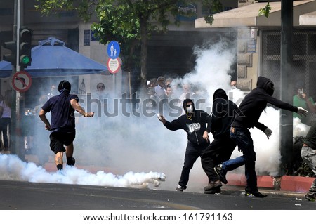 ATHENS, GREECE -MAY 05: Tear gas bombs explodes next to protesters with covered faces who throw stones at riot police during clashes in central Athens, May 05, 2010.