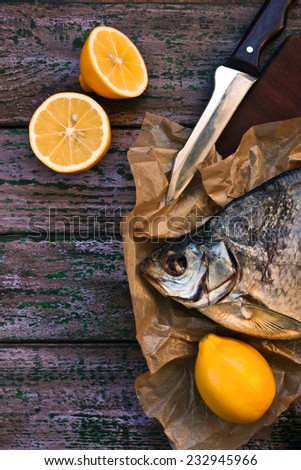 Sun dried fish on the parchment with lemons on the purple wooden table vertical