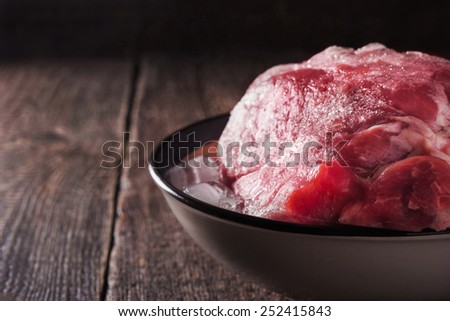 Frozen pork on the plate with ice on the wooden table horizontal