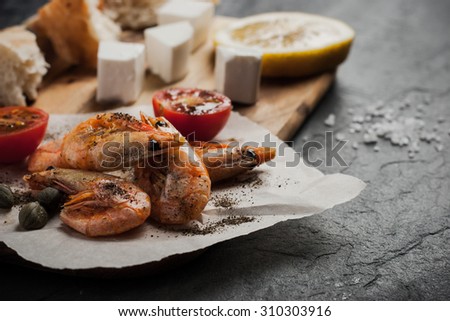 Grilled  shrimps  on the peace of paper with different snack on the black stone table