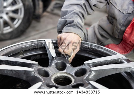 Master body repair man is working on preparing the surface of the aluminum wheel of the car for subsequent painting in the workshop, cleaning and leveling the disk with the help of abrasive material Stock fotó © 