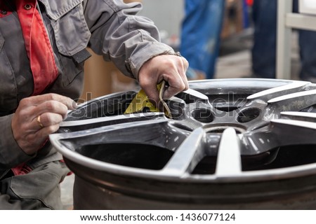 Master body repair man is working on preparing the surface of the aluminum wheel of the car for subsequent painting in the workshop, cleaning and leveling the disk with the help of abrasive material Stock fotó © 