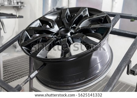 A black painted aluminum alloy wheel is mounted on a special frame during drying in a chamber in a vehicle body repair workshop. Auto service industry. Stock fotó © 