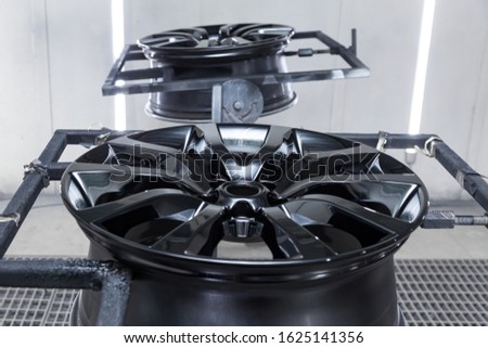 A Two black painted aluminum alloy wheel is mounted on a special frame during drying in a chamber in a vehicle body repair workshop. Auto service industry. Stock fotó © 
