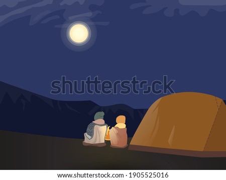 Overnight outdoor camping near the mountains. Campers sitting by a bonfire watching bright full moon next to a tent. Used to portray outdoor activities, families and friends spending time together.
