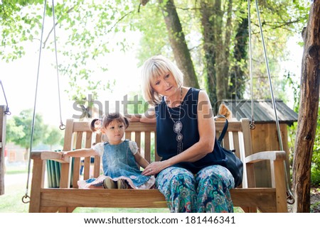 Little girl and her elderly mother are sitting on the bench in the park.