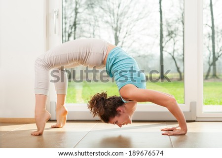 Young woman practicing yoga - Urdhva Dhanurasana / Upward bow pose indoor in fron of the window