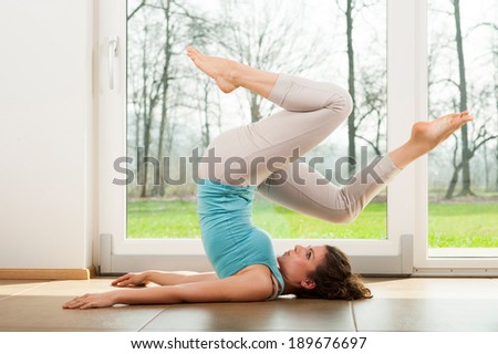 Beautiful young girl doing yoga exercise in front of the window. Human wheel. Indoor.