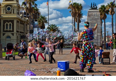 GLENELG, AUSTRALIA - JUNE 6, 2014: A street entertainer performs his bubble show for a group of children.