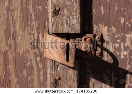 A close up of a hatch lock on an old wood door with peeling paint.