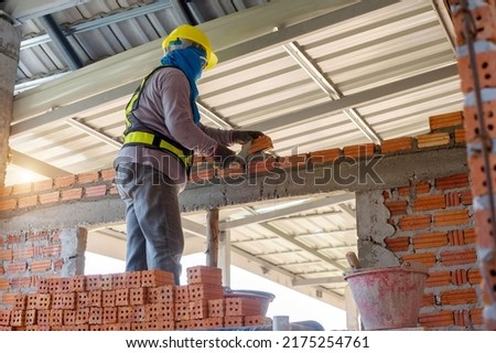 Builder carefully puts red brick on the masonry. Quick work bricklayer. Guy measures level masonry. Man is building brick wall. Correctly calculate material. Builder manually carries brick structure,B Foto stock © 