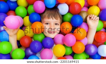 Colorful balls dry pool kindergarten playground child indoor play area. Playroom kids ball pit. Caucasian boy indoor playground kids play zone or kids zone. Smile kid lying colorful plastic balls pool Imagine de stoc © 