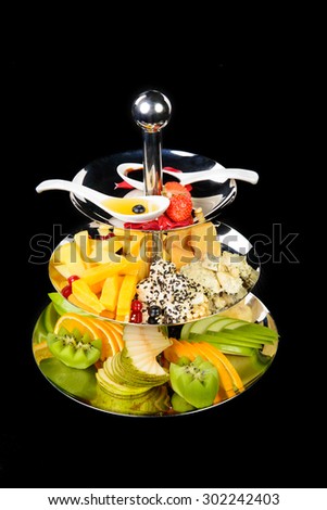 three tier stand with cheese and fruits on black background