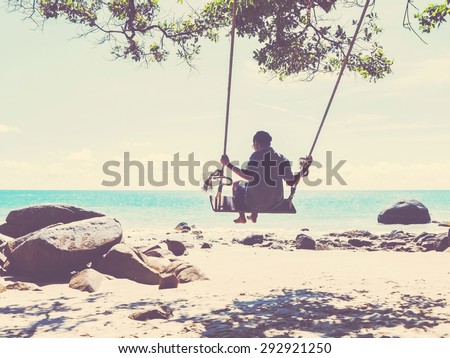Young man swinging in a swing on tropical summer beach, vintage filter effect