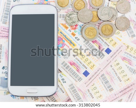 Mobile phone and coins on Thai lottery tickets