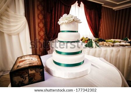White wedding cake with decorative flower at the top is on the table, along with boxes for gifts