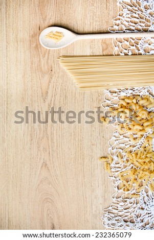Wood spoon, different pasta on knitted tablecloth and wood background