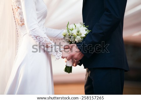 Bride and groom on wedding day. Groom hold on bride\'s hands. Focused on wedding bouquet