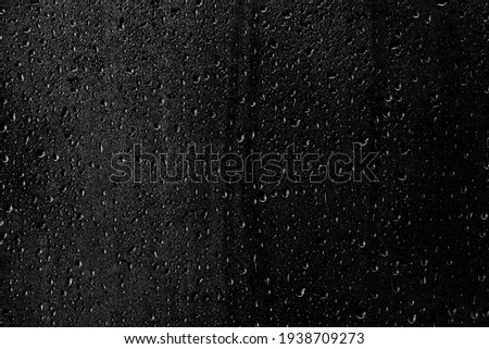 Drops of water flow down the surface of the clear glass on a black background. Texture for creativity.