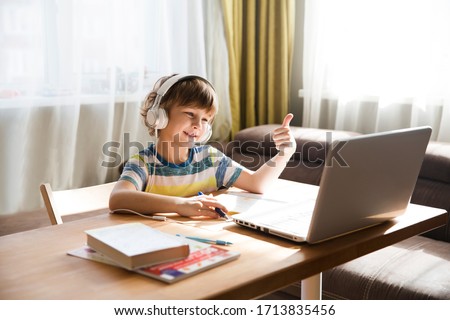 child boy  in headphones  show sight thumbs up, is using a laptop and communicates on the Internet  at home. homeschooling, distant learning, online e