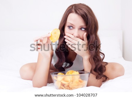 pretty woman eating potato chips in bed at home  and scared of gaining weight