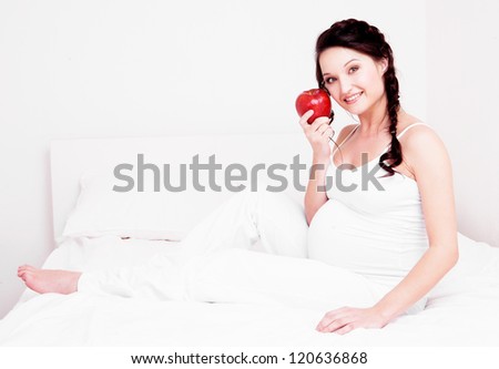 beautiful young pregnant woman eating an apple in bed at home