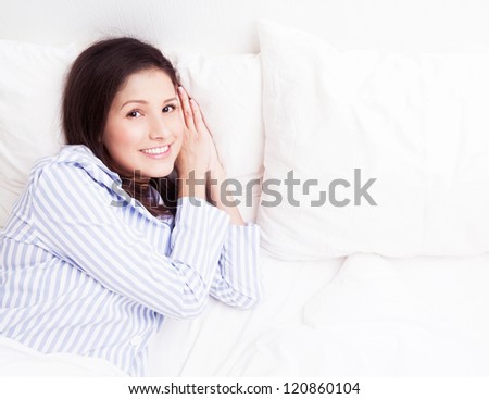 young brunette woman wearing pajamas on the white linen in bed at home, top view
