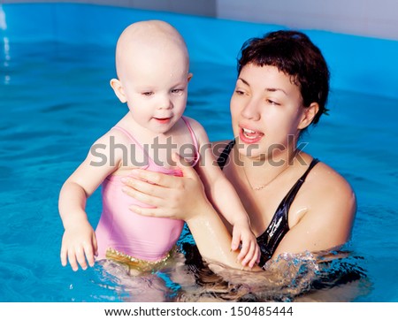 mother teaching her baby swimming in a swimming pool