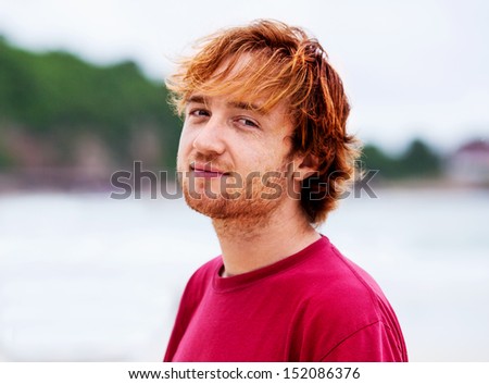 portrait of a young ginger freckled man wearing a red shirt on the beach