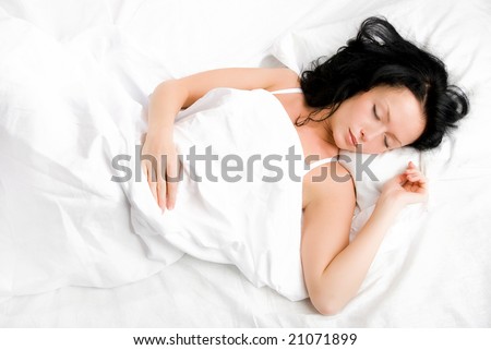 beautiful young brunette woman sleeping peacefully on the white sheets
