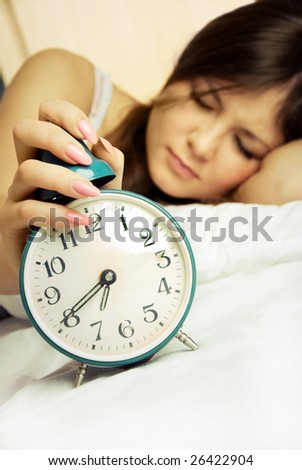 young woman switches off the alarm clock in the morning and keeps sleeping
