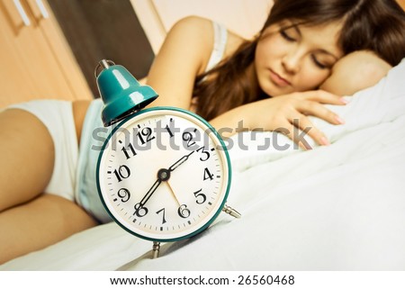 beautiful young brunette woman sleeping peacefully in her bed with the alarm clock standing near her