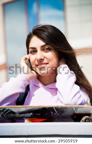 portrait of a pretty teenage girl with a skate board talking on the cellphone outdoor
