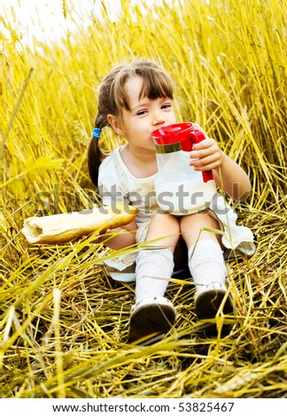 cute little girl in the wheat field eating a long loaf and drinking milk