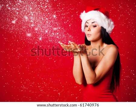 pretty young brunette woman dressed as Santa blowing on the snow on her hands