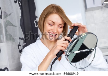 beautiful young woman using a hair straightener at home