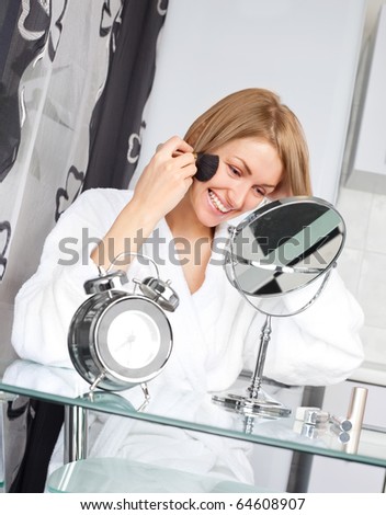 beautiful young woman looking into the mirror and applying powder with a brush