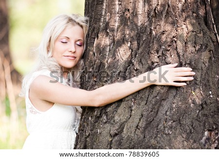 beautiful young blond woman embracing a big tree  on a warm summer day