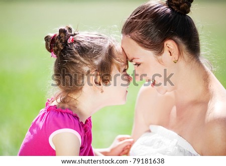 beautiful young mother and her daughter in the park on a sunny summer day talking and laughing (focus on the woman)