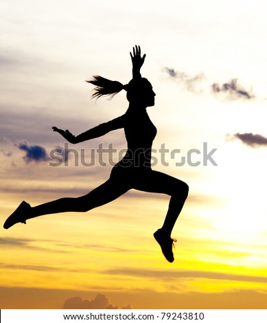 Silhouette of a beautiful jumping woman against yellow sky with clouds at sunset