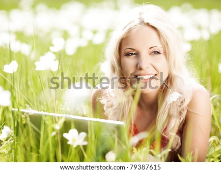 beautiful young blond woman with a laptop  in the park  on a warm summer day