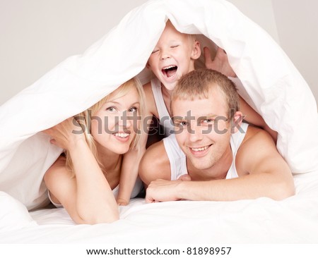 happy family; mother ,father and their son under the blanket in  bed at home