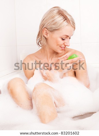 beautiful young blond woman taking a bath with foam and using a homemade glycerin soap