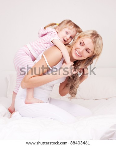 happy young mother playing with her daughter on the bed at home