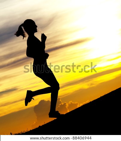 Silhouette of a beautiful woman running up the hill against yellow sky with clouds at sunset
